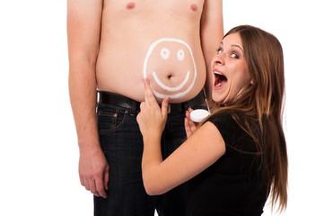girl painting a smiley on her boyfriends belly