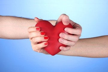 Man and woman holding red heart in hands on blue background