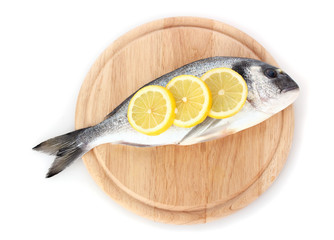 Fresh fish with lemon on wooden cutting board isolated on white.