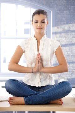 Young female meditating on top of desk