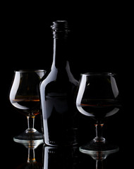 Glasses of brandy and bottle on black background