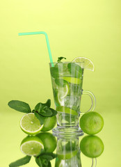 Glass of cocktail with lime and mint on green background
