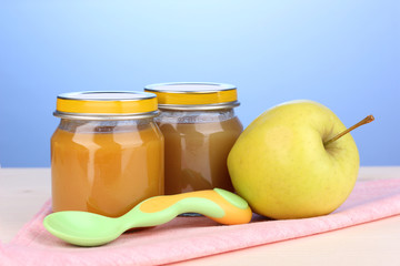 Jars of baby puree with spoon on napkin on blue background