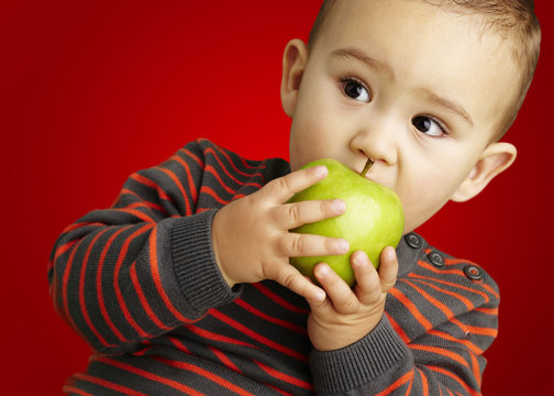 portrait of a handsome kid bitting a green apple over red backgr