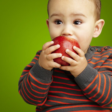 portrait of a handsome kid sucking a red apple over green backgr