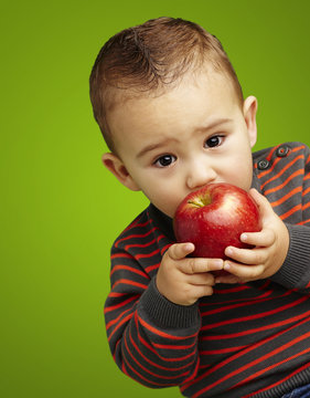portrait of a handsome kid sucking a red apple over green backgr