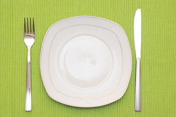 Empty dish, knife and fork and green napkin on wood table