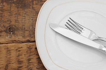 White empty plate with fork and knife on wood table