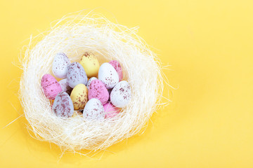 Fototapeta na wymiar Easter eggs in a white nest, on yellow background