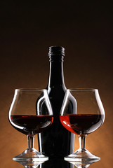 Glasses of brandy and bottle on brown background