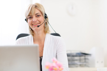 Happy senior business woman with headset working on laptop