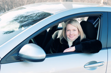 Happy blond woman sitting in her car outdoors and smiling