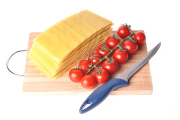 raw lasagna with tomato and knife on the cutting board