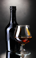 Glass of brandy and bottle on gray background