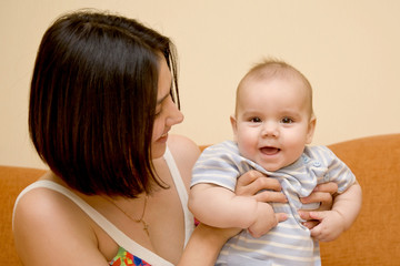 Happy mother and baby with brown eyes sitting on the sofa