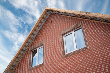 Detail of the facade of a brick house with a roof and windows