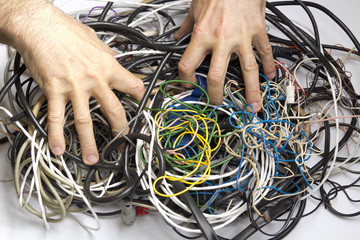 Two male hands rummage among  tangle of cables and wires