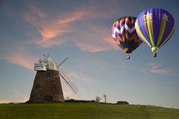 Fototapeta na wymiar Traditional old windmill at sunset with hot air balloons