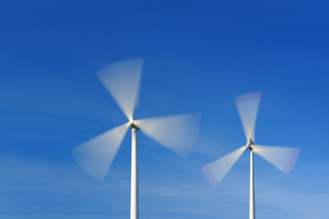 Two wind turbines in movement against blue sky