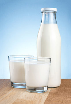 Full Bottle of fresh milk and two glass is wooden table on a blu