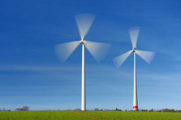 Two wind turbines in movement on a green field