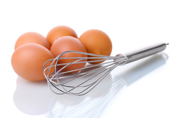 Metal whisk for whipping eggs and brown eggs isolated on white