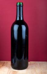 Weinflasche auf Holzplatte vor rotem Hintergrund