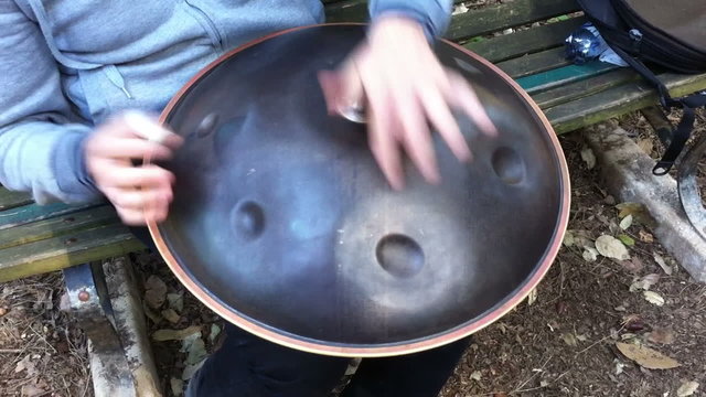 A guy playing hang drum on a bench