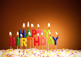 Happy birthday lit candles on brown background