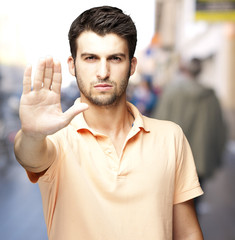 portrait of a comely young man doing stop symbol at a crowded st