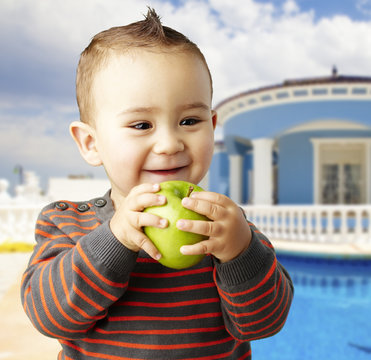 portrait of funny kid holding green apple and smiling at home