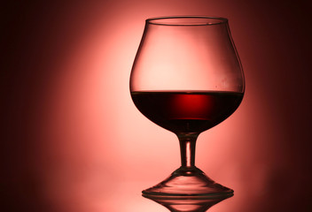 Glass of cognac on red background