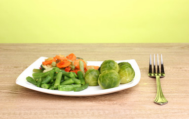 Mixed vegetables on plate on wooden table on green background