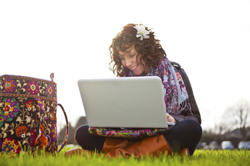 Beautiful young student using laptop on grass