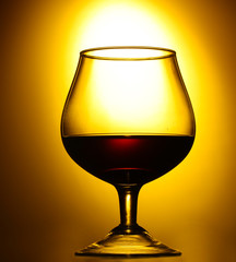 Glass of cognac on yellow background