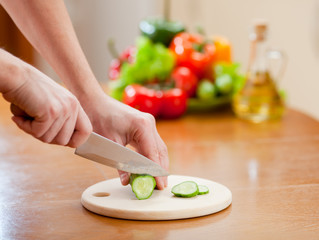 Cutting of cucumber on hardboard and fresh vegetables
