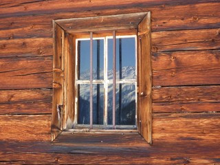 Die Alpen spiegeln sich im Holzfenster der Almhütte