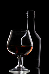 Glass of brandy and bottle on black background
