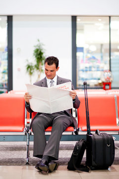 young businessman reading newspaper at airport