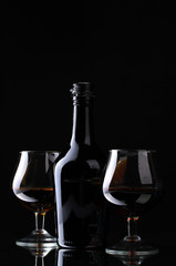 Glasses of brandy and bottle on black background