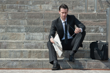 Young business man with newspaper sitting on the stairs.