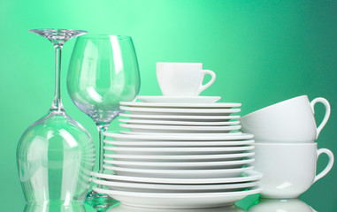 Clean plates, cups and glasses on green background