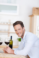 lächelnder mann mit rotwein in der küche