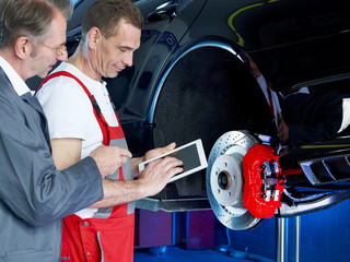 Master mechanic and worker inspecting a car with touchpad