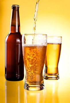 Beer Being Poured in Two glasses and Bottle on yellow background