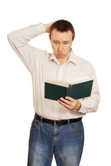 Man with astonishment looks in the book and scratches a nape