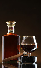 Obraz na płótnie Canvas butelka i kieliszek brandy i cygar na brązowym tle
