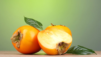 Appetizing persimmons on wooden table on green background