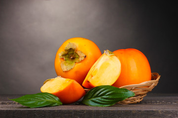 Fototapeta na wymiar Appetizing persimmons in pad on wooden table on grey background