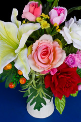 Artificial flowers in a vase on a blue background.